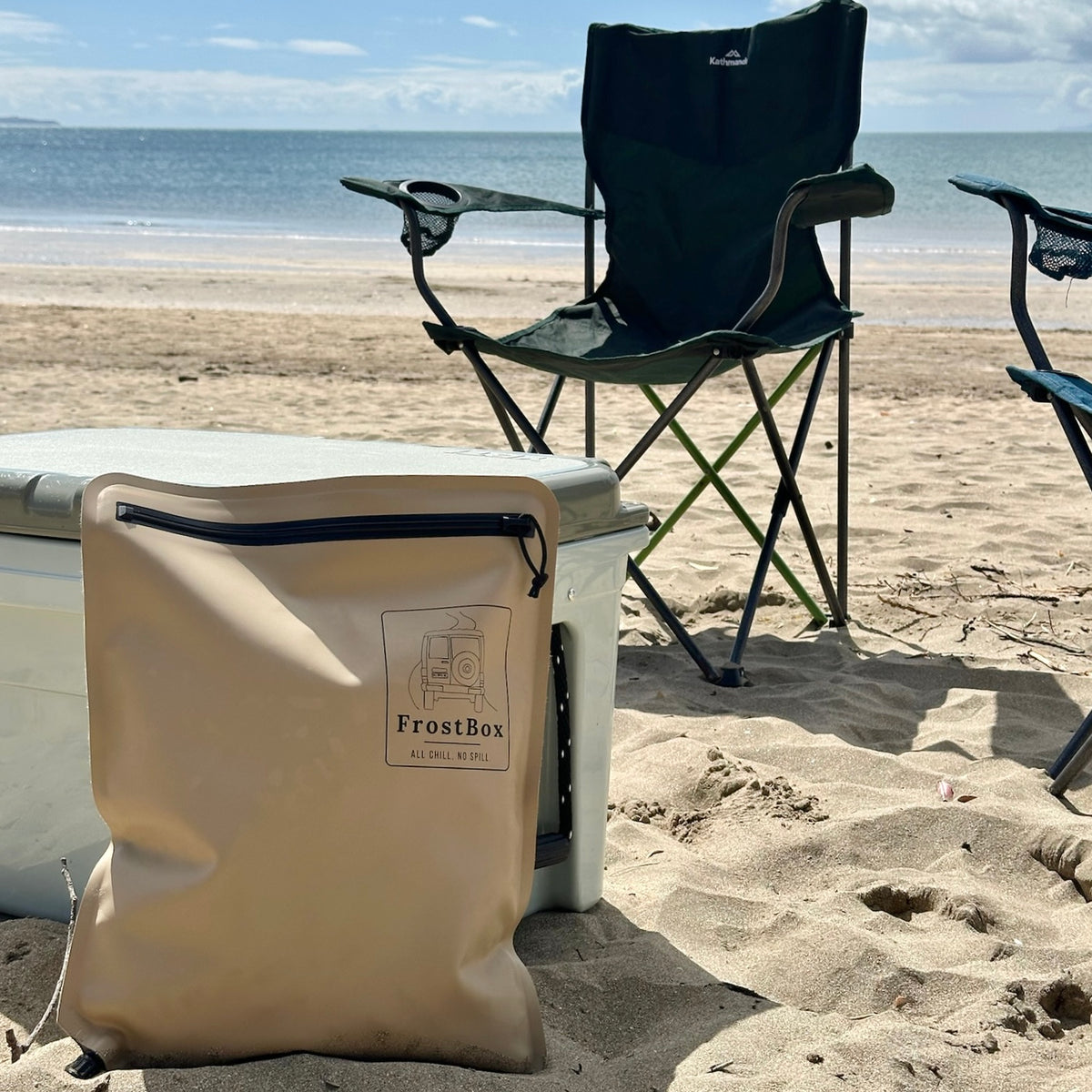 Sand FrostBox ice bag against a chilly bin on the beach with camping chairs