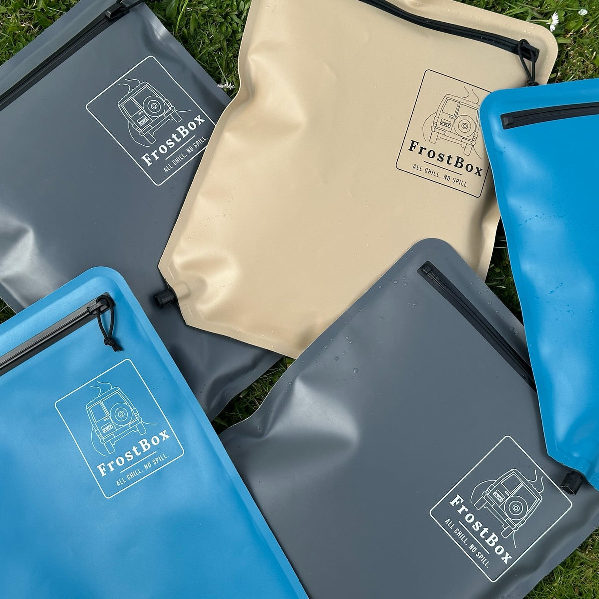 FrostBox ice bags in Sand, Charcoal and Tasman Blue laid out on the grass